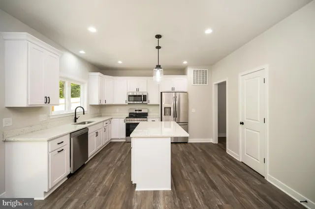 a kitchen with stainless steel appliances a stove top oven a sink a refrigerator white cabinets and wooden floor