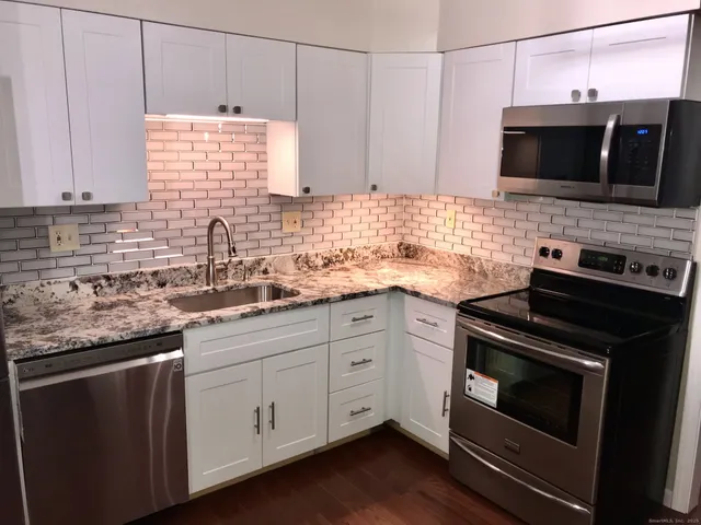 a kitchen with stainless steel appliances white cabinets granite counter tops and a wooden floors