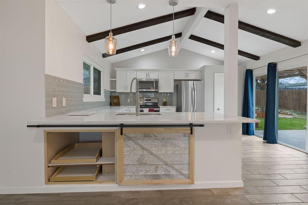 5211 Halmark Drive Austin, TX 78723 - Photo 7 of 27 Modern kitchen with vaulted ceilings, exposed beams, and a stylish barn-door island feature.