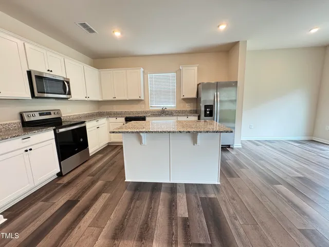 a large kitchen with stainless steel appliances granite countertop a stove a sink dishwasher and a refrigerator with wooden floor