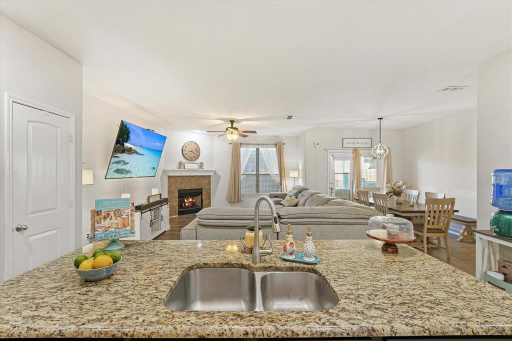 3801 Surf Street Denton, TX 76208 - Photo 28 of 29 Kitchen featuring open floor plan, ceiling fan, a center island with sink, light stone countertops, and a tiled fireplace