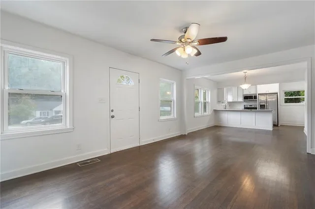 a view of a livingroom with wooden floor a ceiling fan and windows