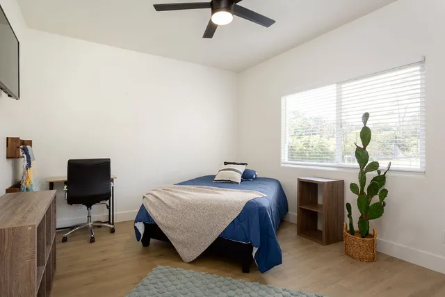 a bedroom with a bed table chair and a window