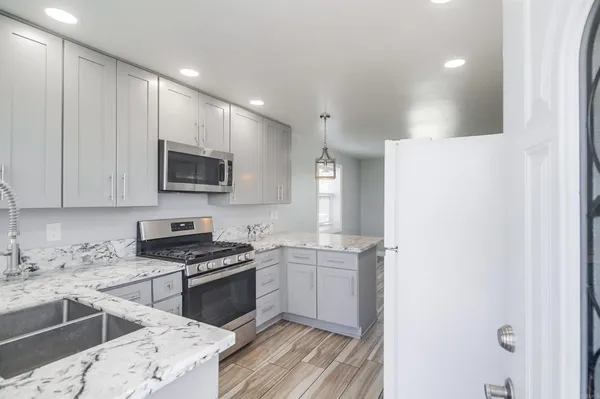 a kitchen with stainless steel appliances granite countertop a refrigerator a sink dishwasher a stove and white cabinets with wooden floor