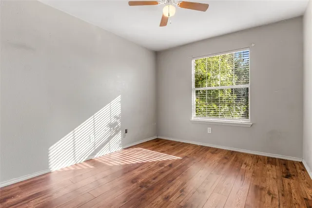 an empty room with wooden floor chandelier fan and windows