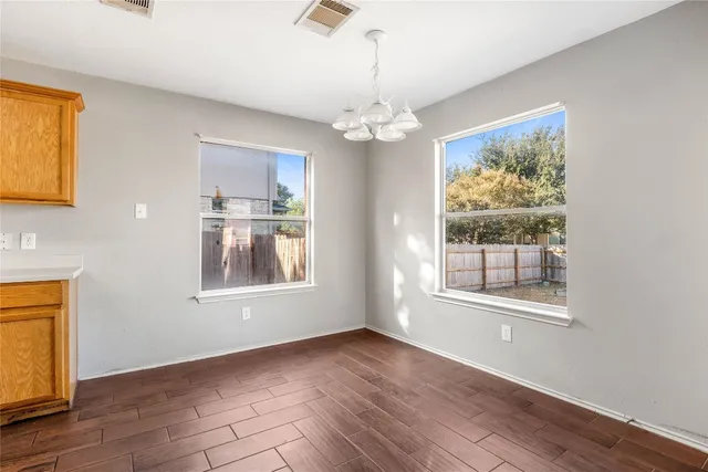 an empty room with wooden floor chandelier and windows