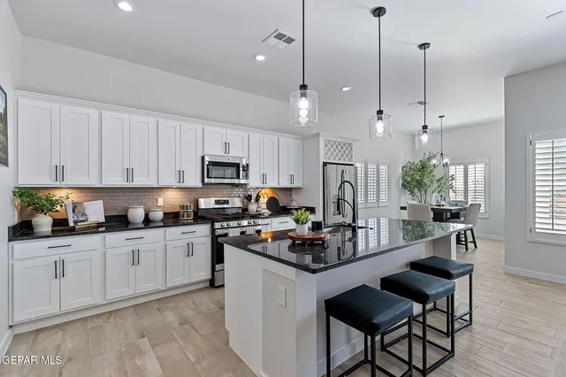 a kitchen with stainless steel appliances granite countertop a sink a stove a refrigerator cabinets a dining table and chairs