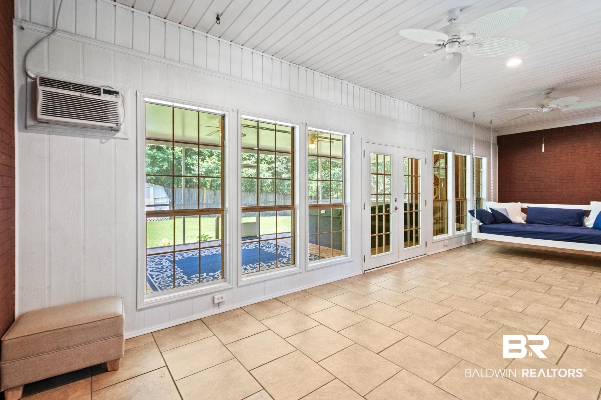3176 Cedar Court Mobile, AL 36619 - Photo 25 of 33 Enclosed porch featuring tile flooring, white vertical wall paneling, multiple windows, and a brick accent wall