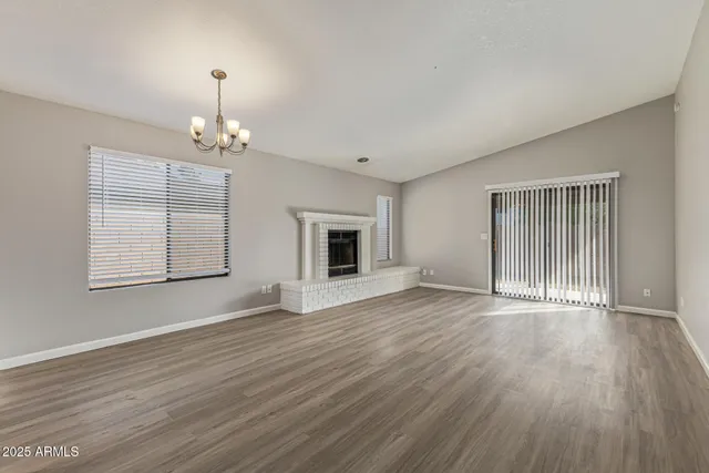 an empty room with wooden floor chandelier and windows