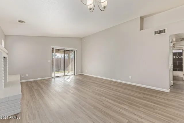 an empty room with wooden floor chandelier and windows