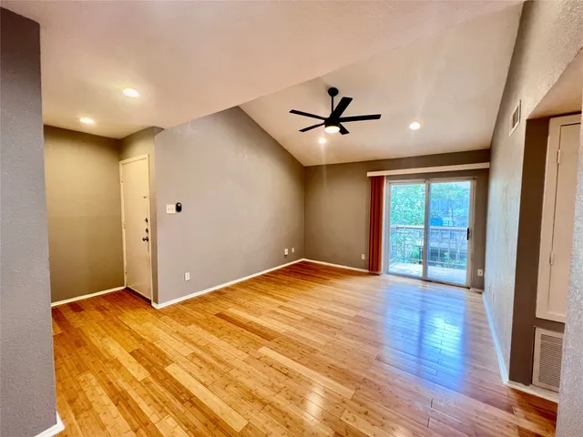 a view of empty room with wooden floor and fan
