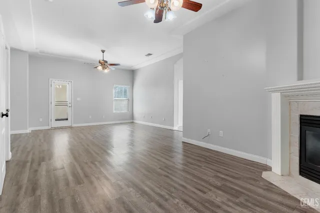 an empty room with wooden floor chandelier fan and windows