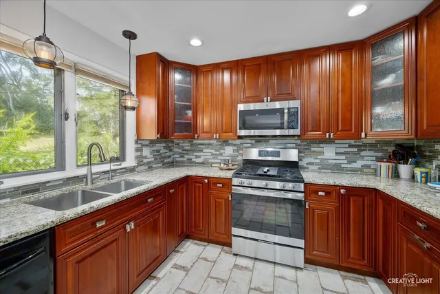 a kitchen with stainless steel appliances granite countertop wooden cabinets a stove top oven a sink and dishwasher with wooden floor