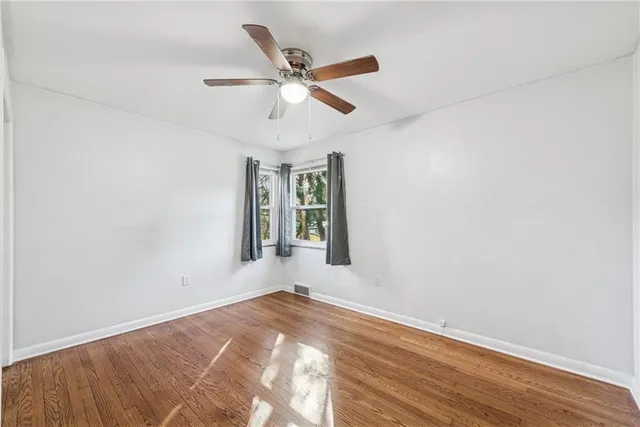 an empty room with wooden floor fan and windows