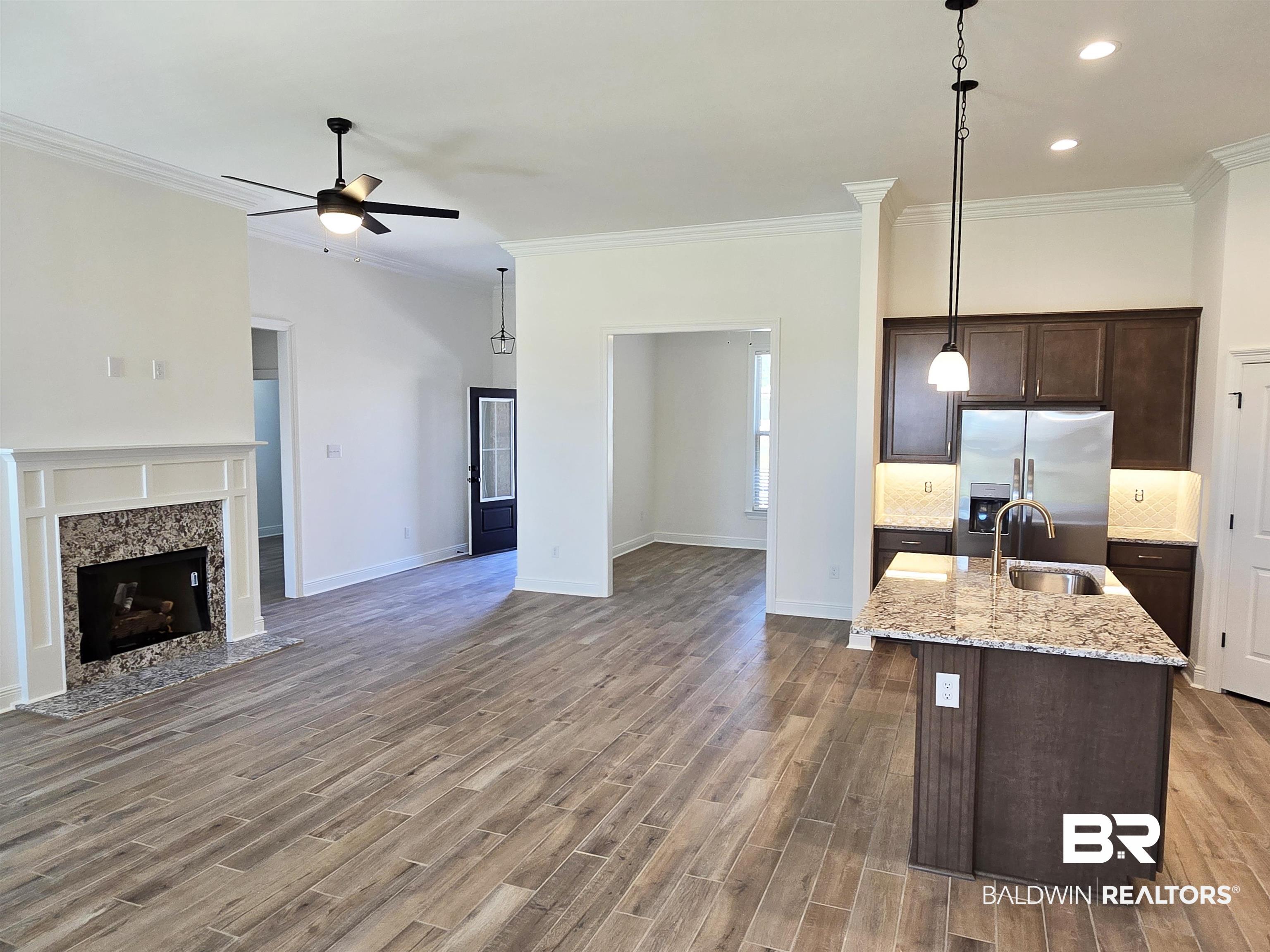 11178 Bonaventure Avenue Daphne, AL 36526 - Photo 6 of 20 Kitchen with dark wood finish cabinets, a center island with sink, stainless steel fridge, light stone counters, and backsplash