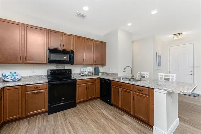 a kitchen with stainless steel appliances granite countertop wooden cabinets a sink a stove a refrigerator and dishwasher with wooden floor