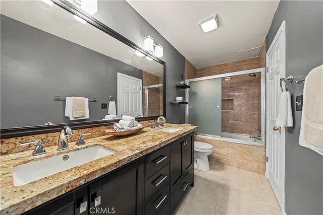 a bathroom with a granite countertop sink a toilet a mirror and shower