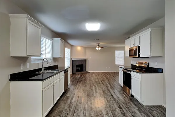 a kitchen with granite countertop a stove top oven a sink dishwasher and white cabinets with wooden floor