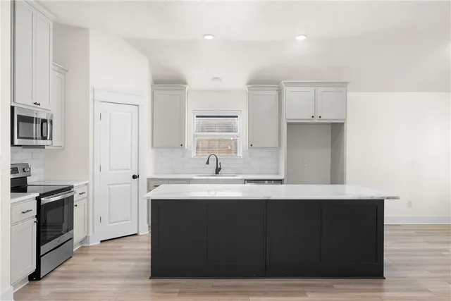 a kitchen with stainless steel appliances granite countertop a sink a stove a refrigerator and white cabinets