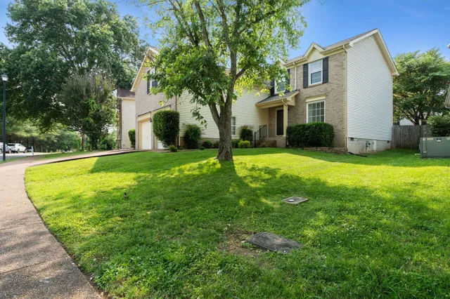 a view of a white house with a big yard plants and large trees