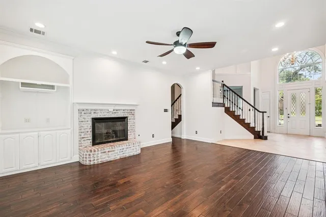a view of a livingroom with wooden floor a fireplace a ceiling fan and windows