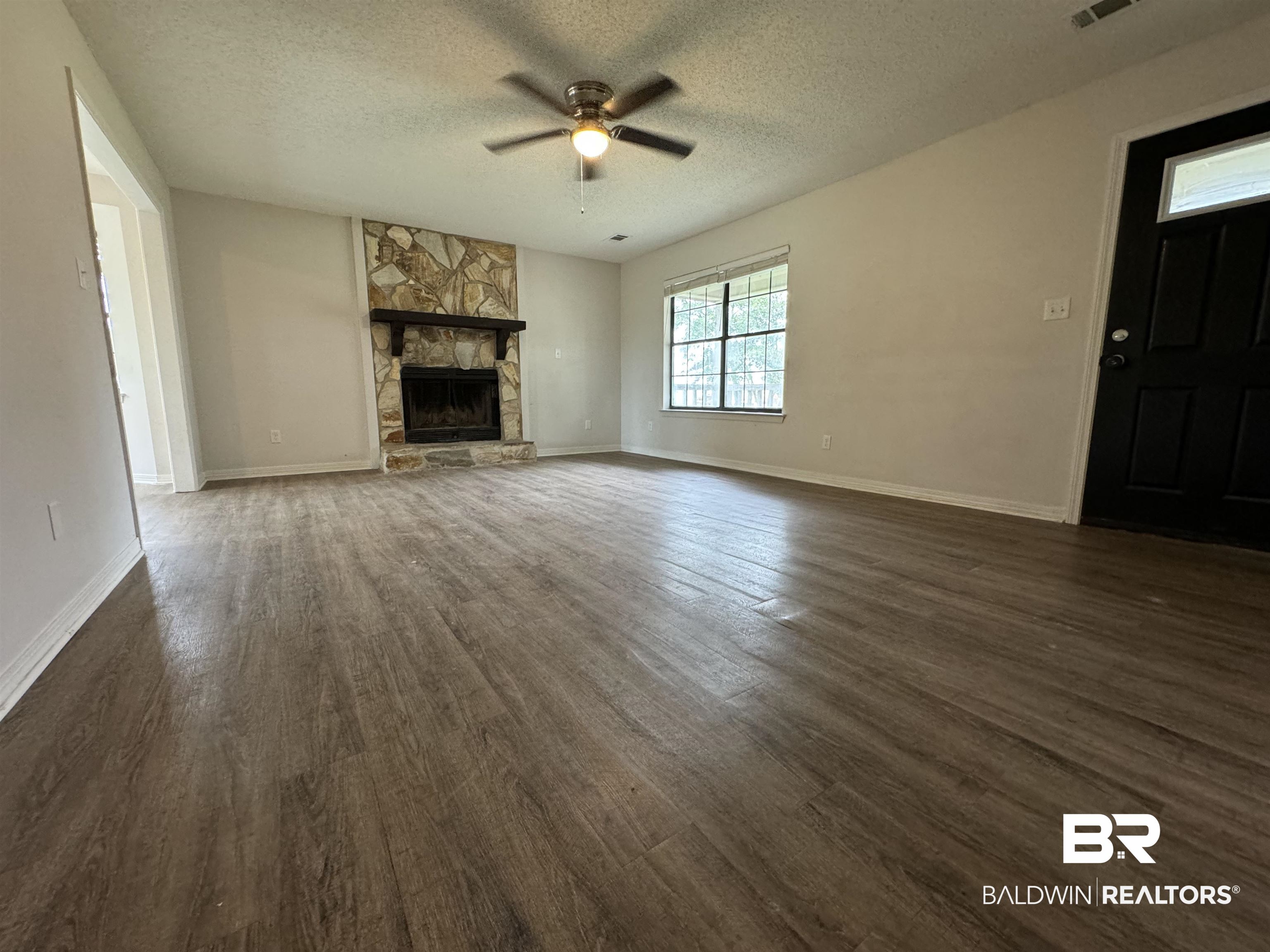 70 Plum Street Uriah, AL 36480 - Photo 4 of 36 Unfurnished living room with ceiling fan, a textured ceiling, dark hardwood / wood-style floors, and a fireplace