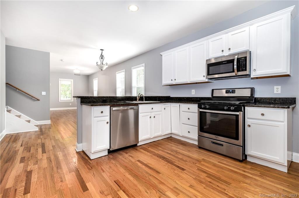 a kitchen with stainless steel appliances white cabinets a sink a stove a microwave and wooden floors