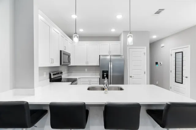 a kitchen with stainless steel appliances a sink a stove a refrigerator cabinets and chairs