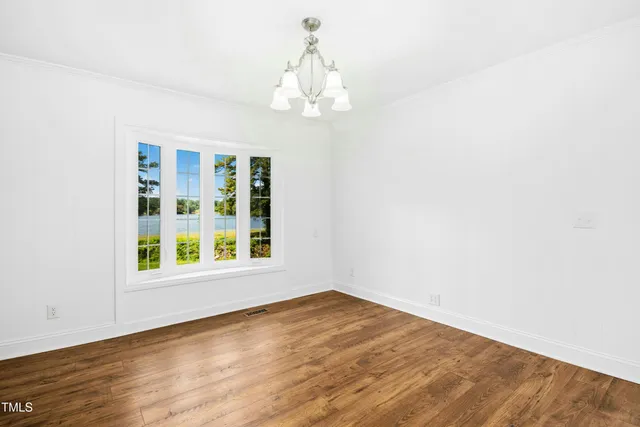 an empty room with wooden floor chandelier and windows