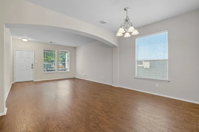 an empty room with wooden floor chandelier and windows