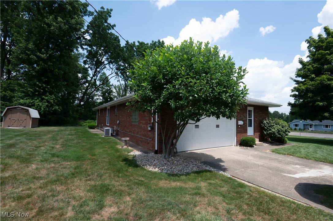 View of property exterior with brick siding, a shed, driveway, a lawn, and a garage