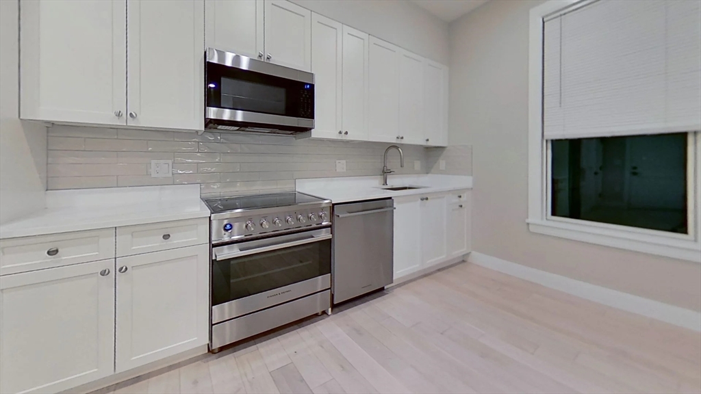197 Green Street, Unit 207 Boston, MA 02130 - Photo 1 of 4 a kitchen with stainless steel appliances white cabinets and a stove top oven