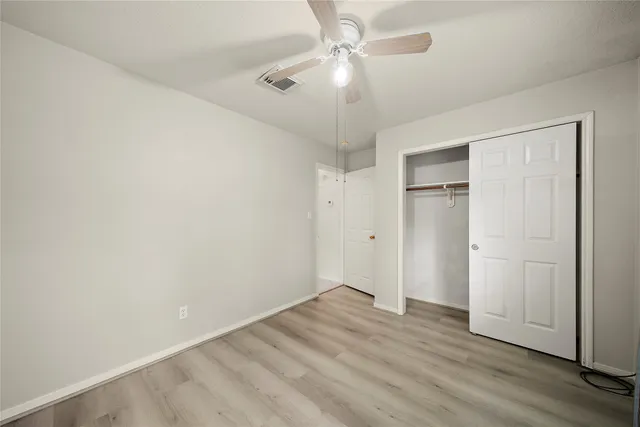 an empty room with wooden floor ceiling fan and window