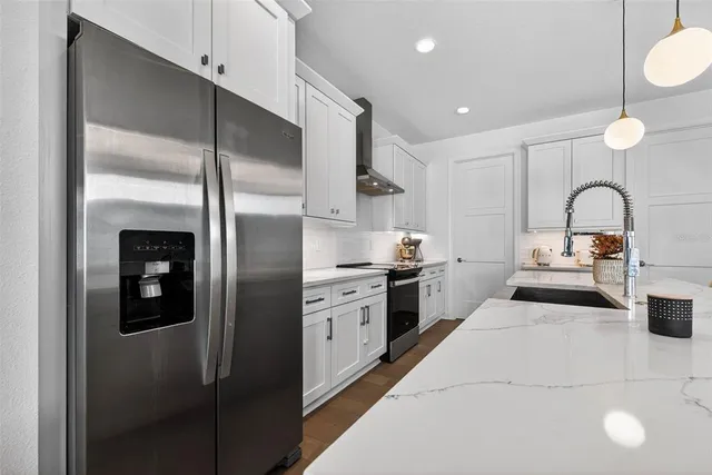 a kitchen with stainless steel appliances kitchen island granite countertop a refrigerator a sink a stove and white cabinets with wooden floor