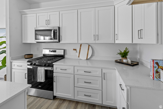1264 West 500 South, Unit 320 Logan, UT 84321 - Photo 9 of 39 Modern kitchen featuring white shaker cabinetry, light-toned countertops, stainless steel appliances, wood-finish flooring, and contemporary hardware