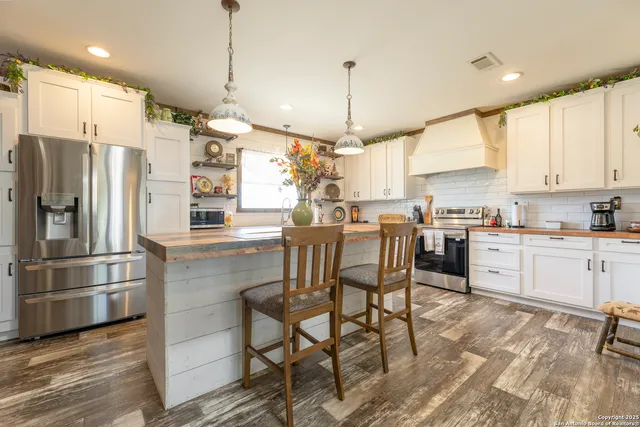 a kitchen with stainless steel appliances granite countertop a refrigerator a sink dishwasher a stove and white cabinets with wooden floor