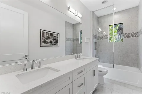 a bathroom with a double vanity sink a toilet a shower and a mirror