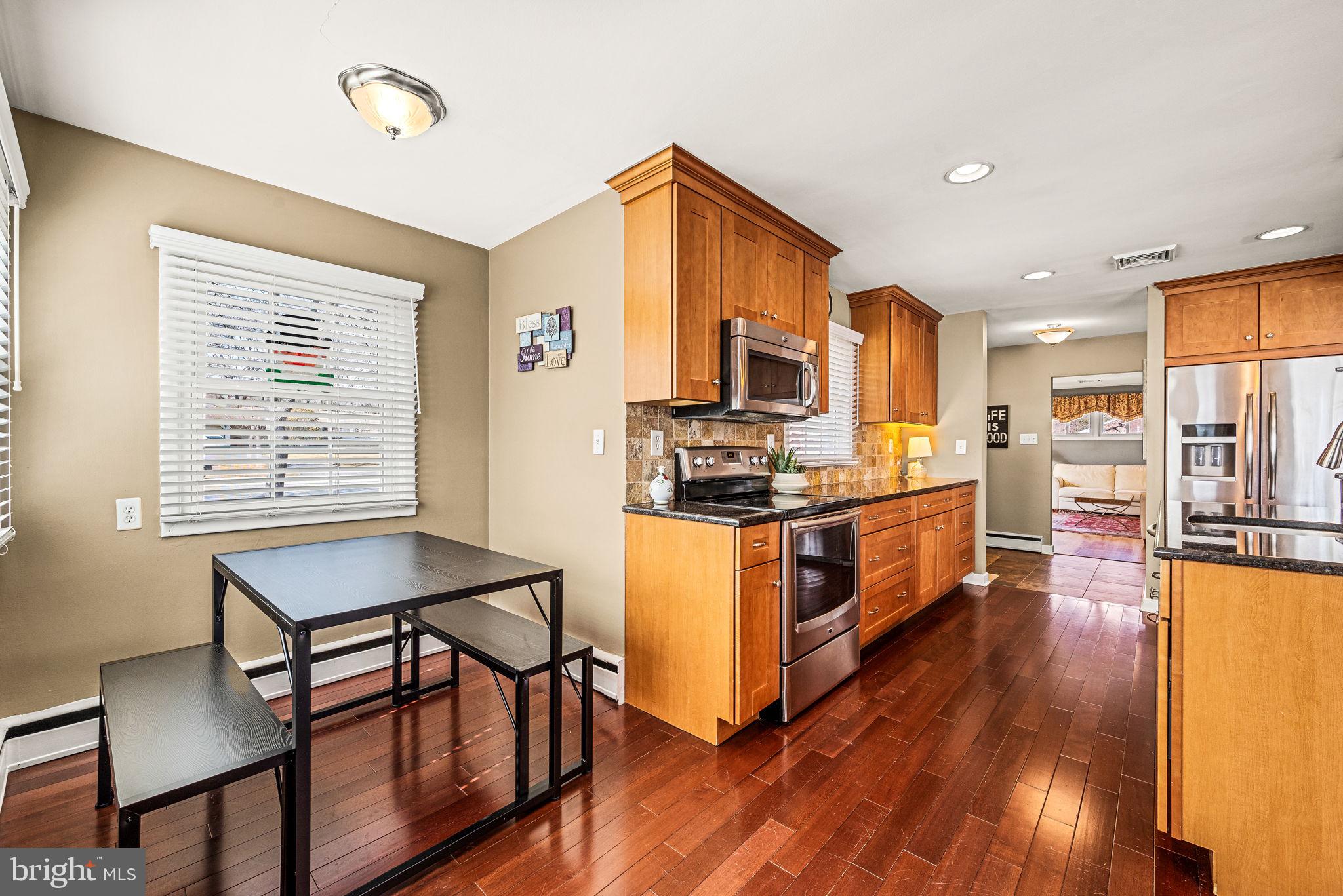 408 Scott Lane Wallingford, PA 19086 - Photo 11 of 39 a kitchen with stainless steel appliances kitchen island granite countertop a stove top oven a sink a dining table and chairs with wooden floor