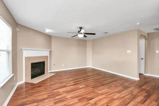 a view of an empty room with wooden floor fireplace and a window