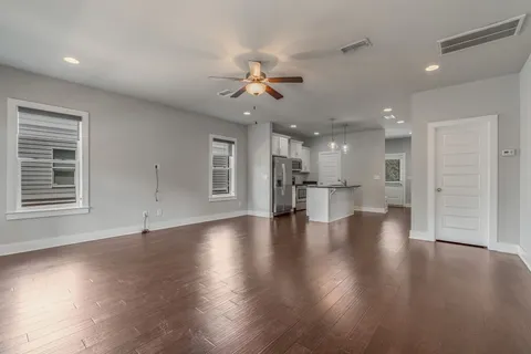an empty room with wooden floor a ceiling fan and kitchen view