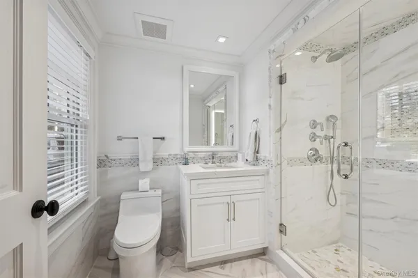 a bathroom with a granite countertop sink a toilet a mirror and shower