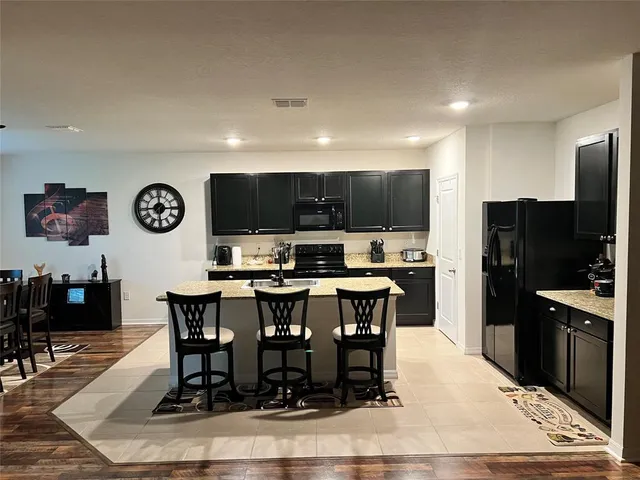 a kitchen with stainless steel appliances kitchen island granite countertop a dining table chairs refrigerator and microwave