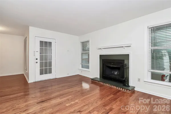 a view of an empty room with wooden floor fireplace and a window
