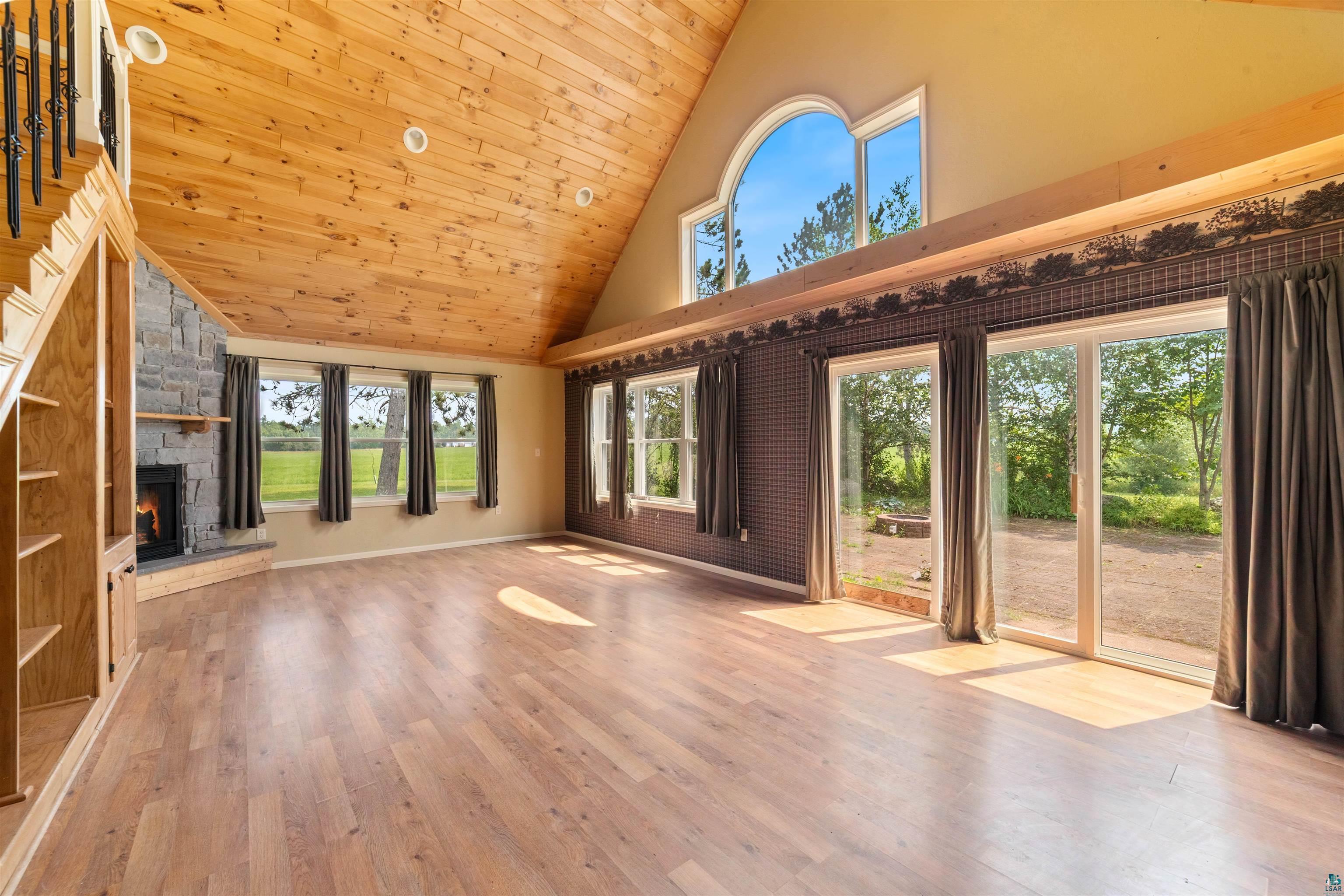 9372 McCamus Road Brookston, MN 55711 - Photo 12 of 49 Unfurnished living room with wooden ceiling, high vaulted ceiling, a stone fireplace, wood finished floors, and healthy amount of natural light