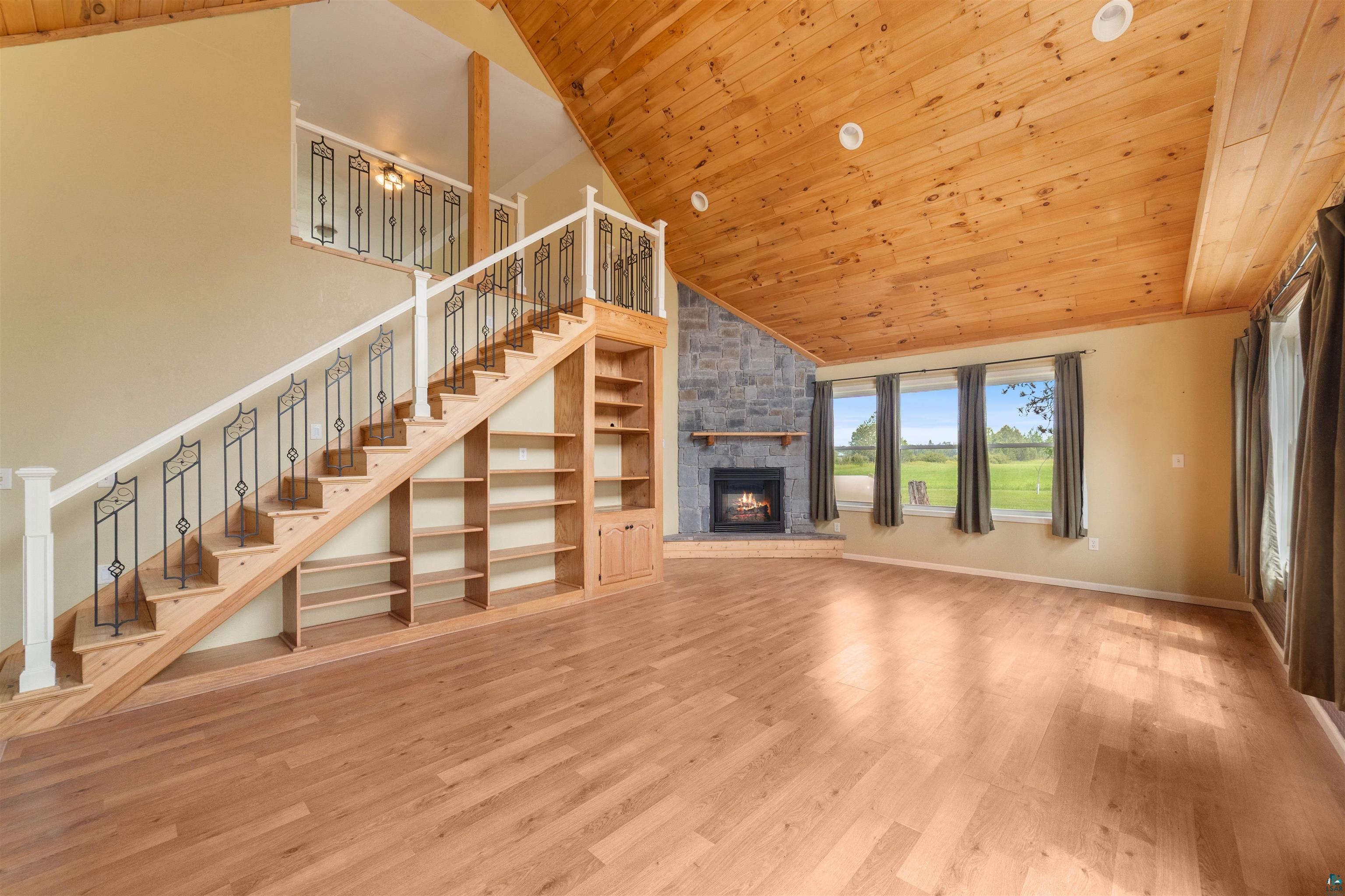 9372 McCamus Road Brookston, MN 55711 - Photo 13 of 49 Unfurnished living room featuring wooden ceiling, a fireplace, wood finished floors, stairway, and high vaulted ceiling