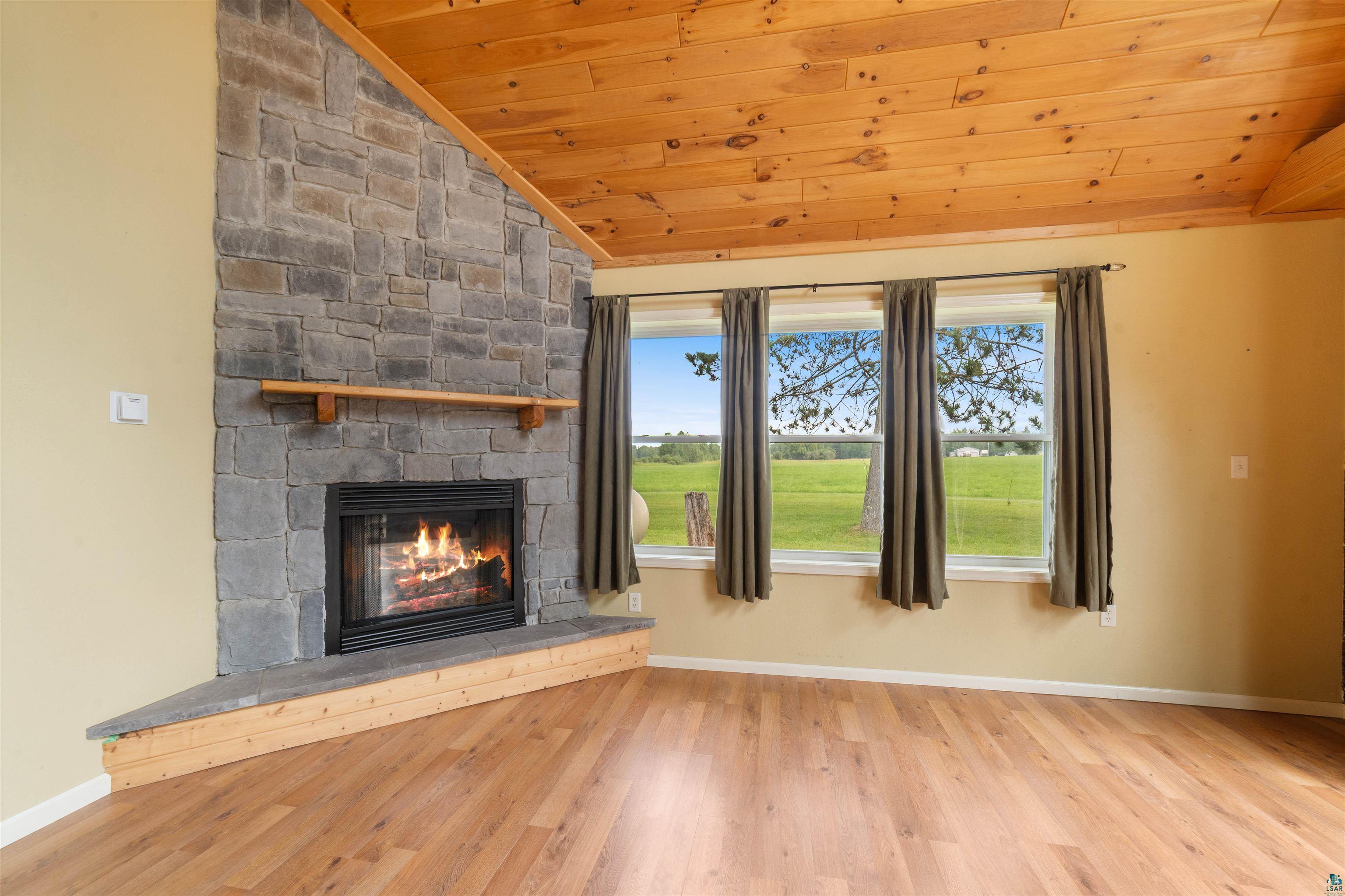 9372 McCamus Road Brookston, MN 55711 - Photo 14 of 49 Unfurnished living room featuring lofted ceiling, a stone fireplace, wood ceiling, and wood finished floors