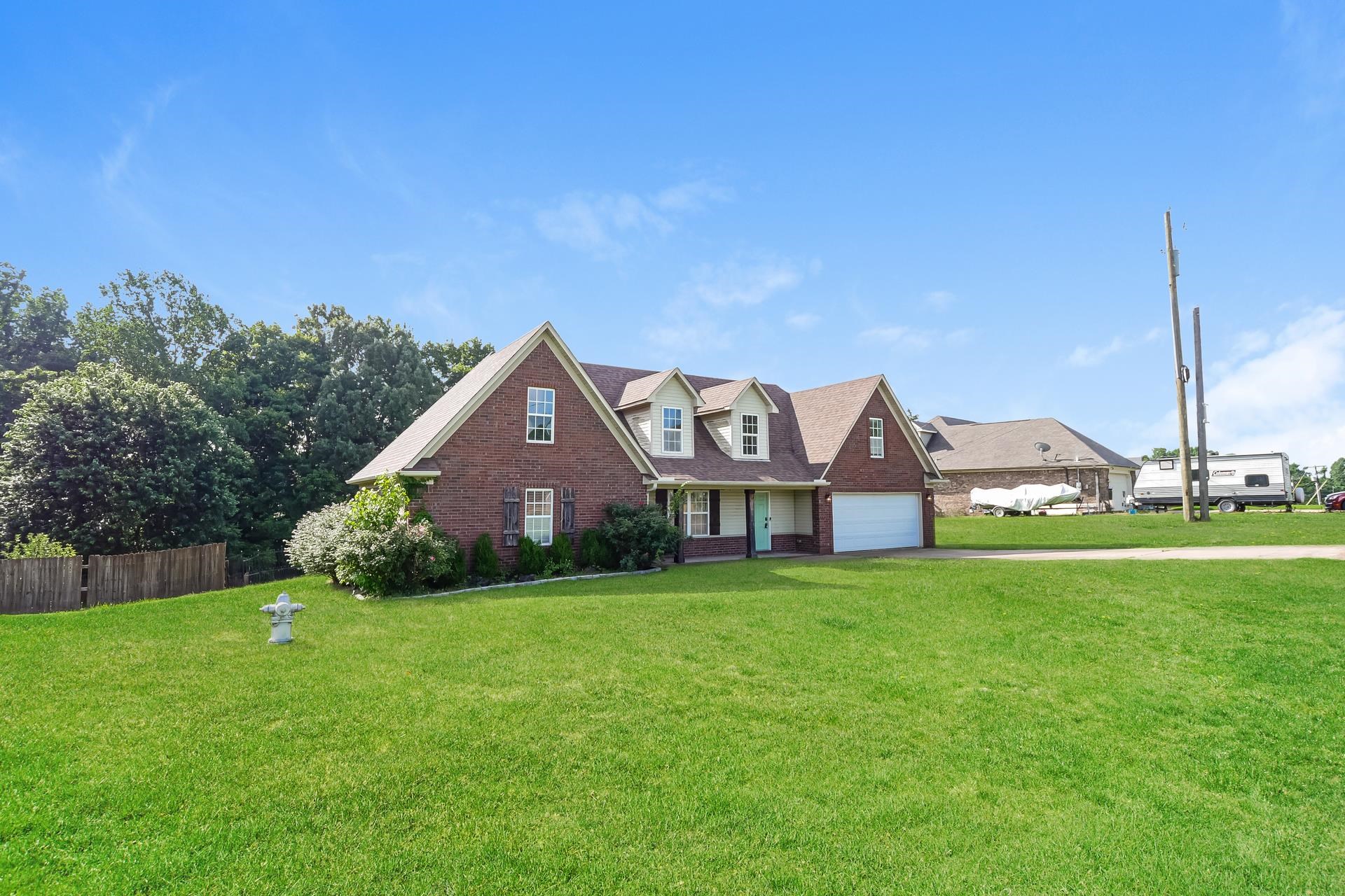 188 David Reed Drive Munford, TN 38058 - Photo 2 of 20 Traditional brick home featuring a two-car garage, dormer windows, a light blue entry door, and a sprawling green lawn