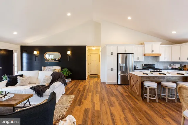 a living room with stainless steel appliances furniture a rug and a kitchen view