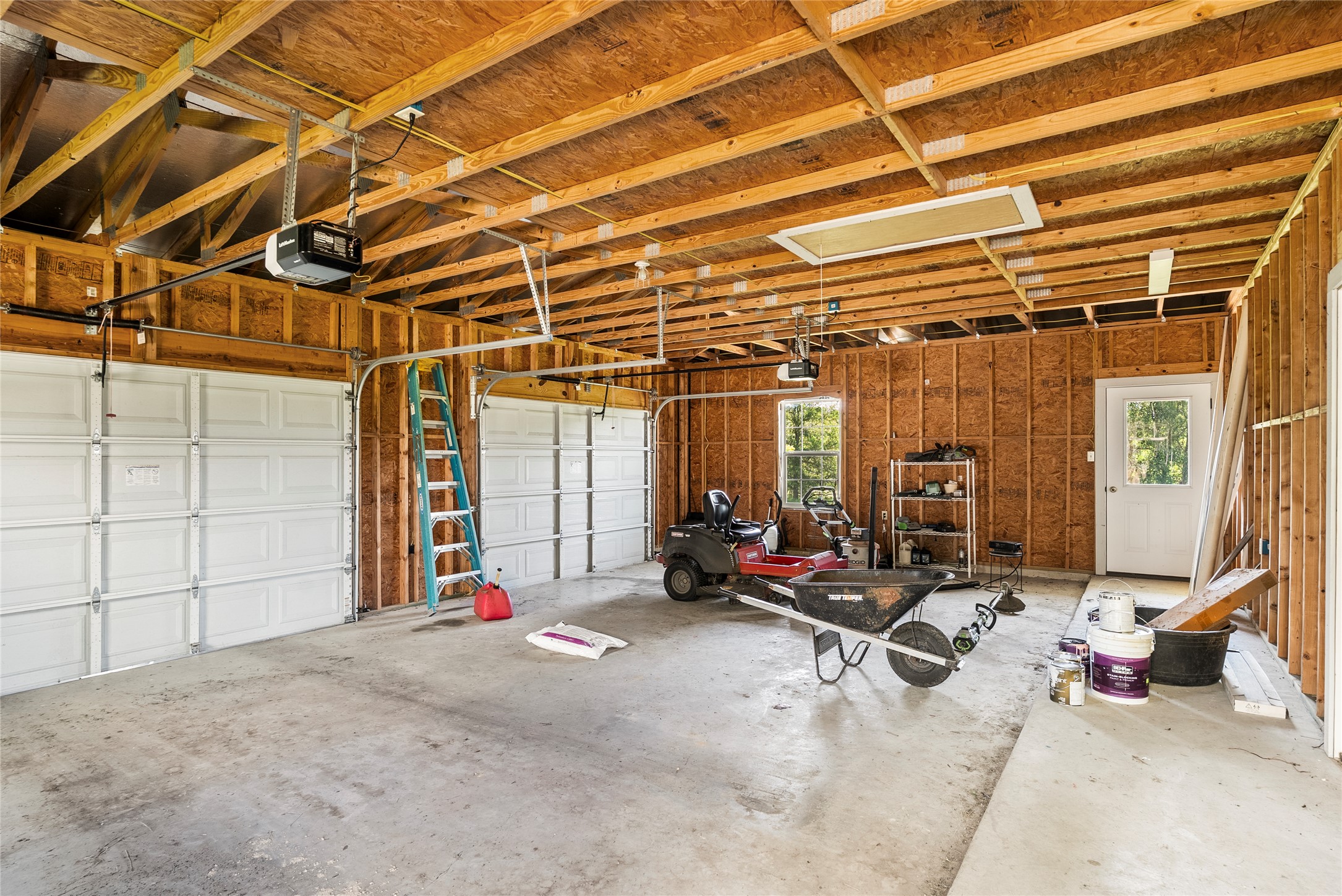 928 Upper Elgin River Road Elgin, TX 78621 - Photo 31 of 40 Spacious garage featuring a concrete floor, exposed wood ceiling joists, and two white overhead doors with automatic openers.