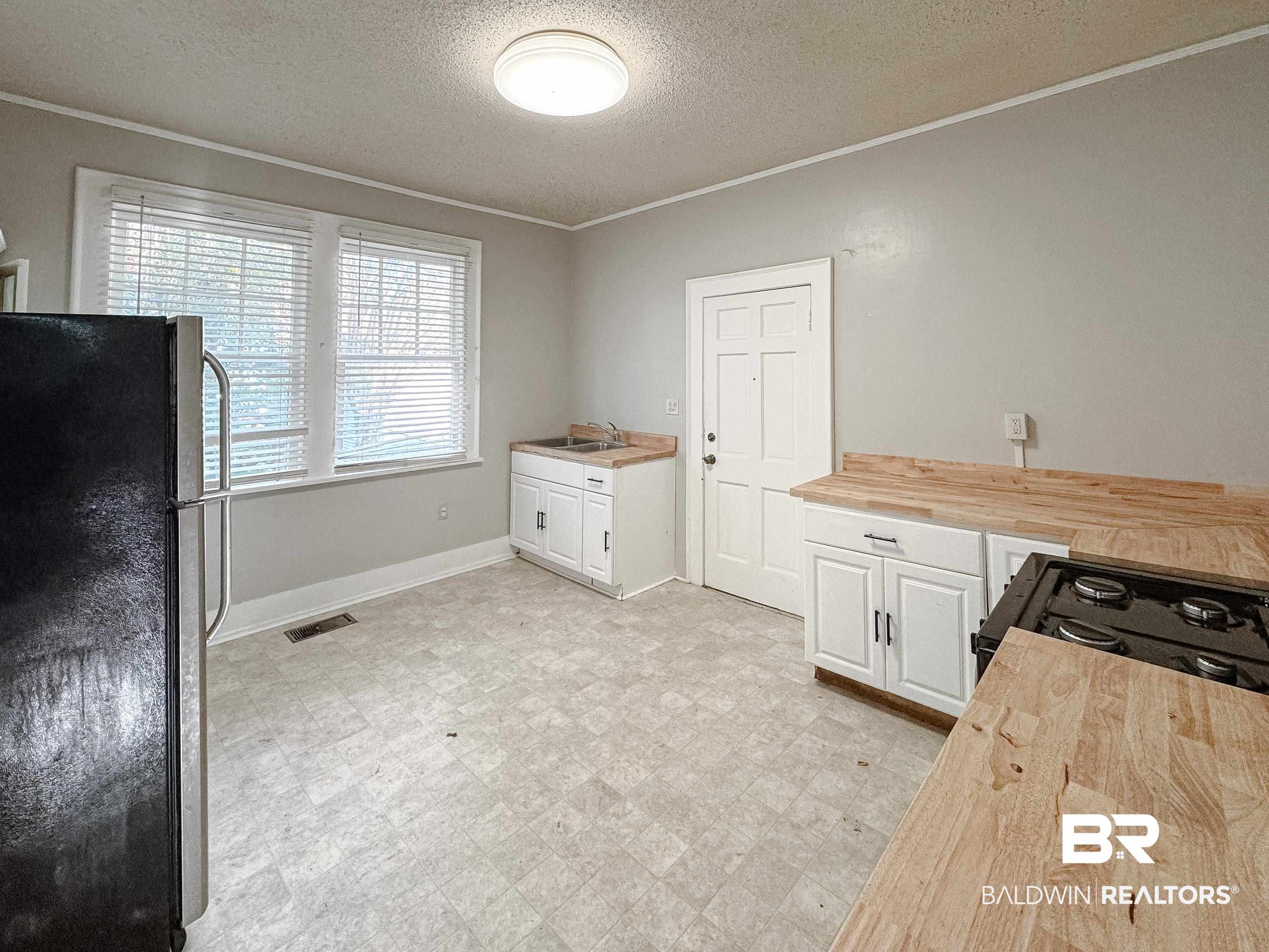 206 1st Street Mobile, AL 36611 - Photo 10 of 26 Kitchen featuring butcher block countertops, white cabinets, freestanding refrigerator, a textured ceiling, and ornamental molding